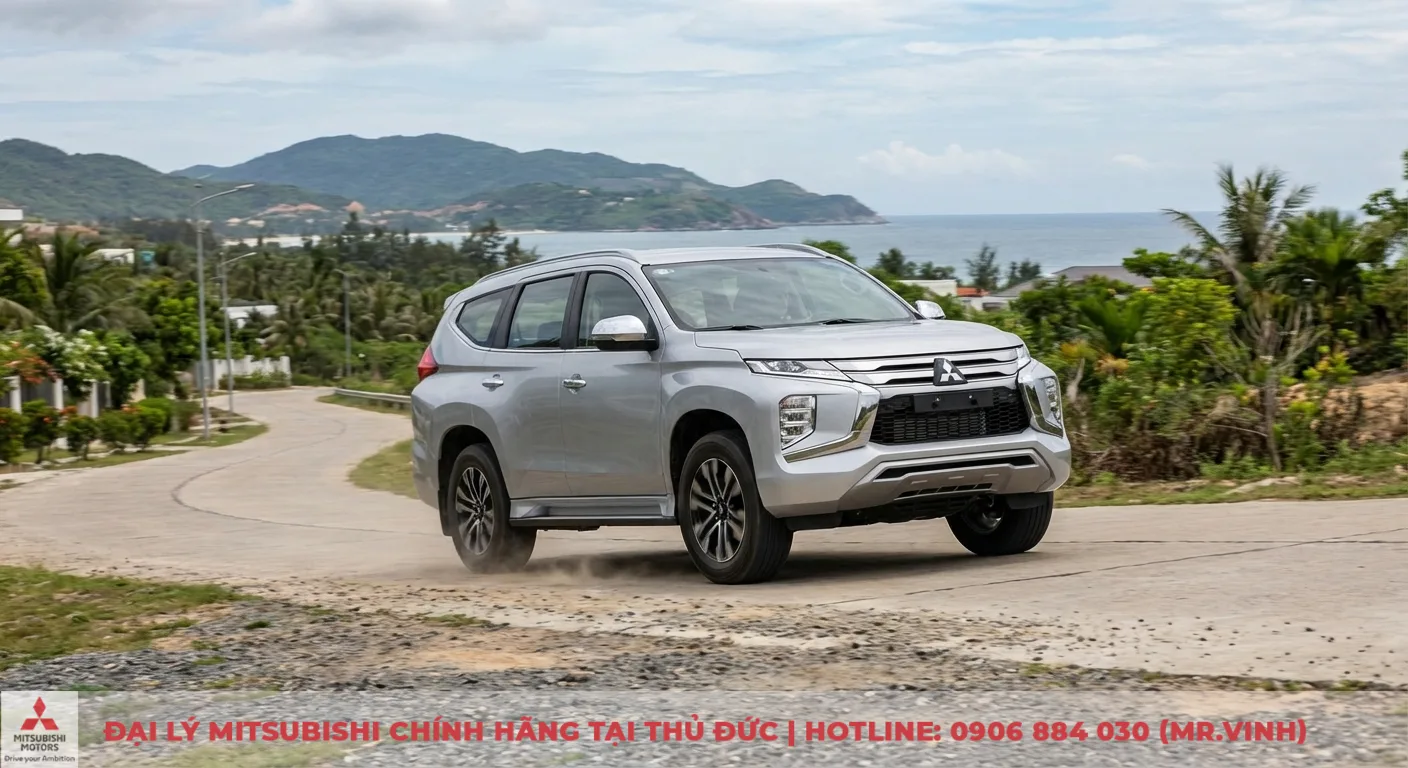 Xe SUV m&agrave;u bạc của Mitsubishi đang di chuyển tr&ecirc;n đường cong ven biển, bụi đất bắn ra từ b&aacute;nh xe thể hiện khả năng xử l&yacute; tr&ecirc;n địa h&igrave;nh